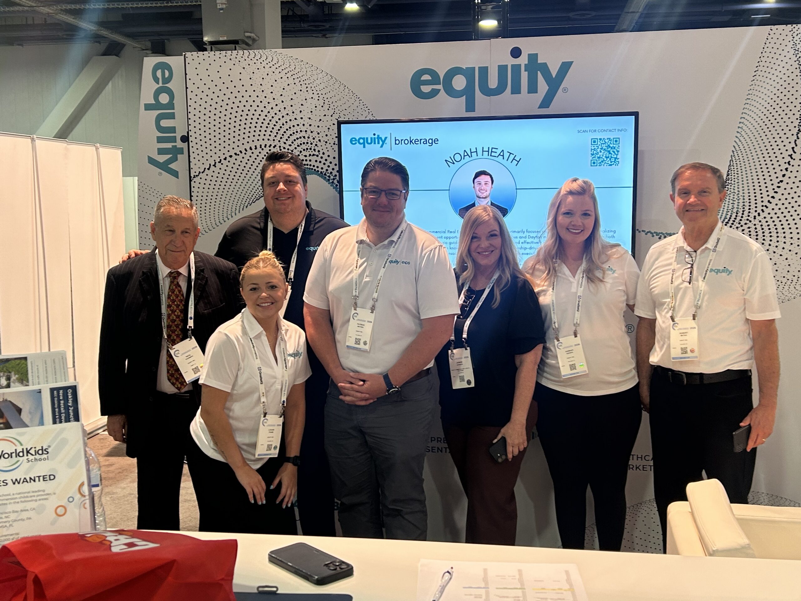 Equity team members gathered at their brokerage booth showcasing Noah Heath's profile at a commercial real estate conference