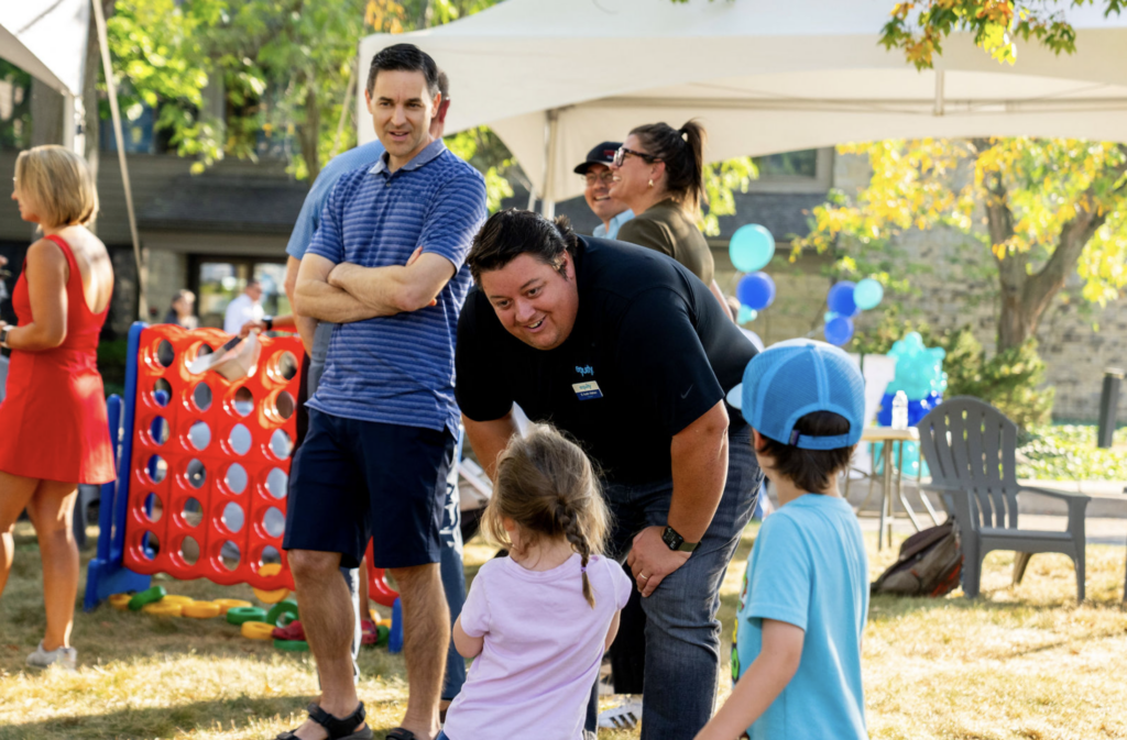 Equity team member interacting with children at an outdoor community event with lawn games and balloon decorations.
