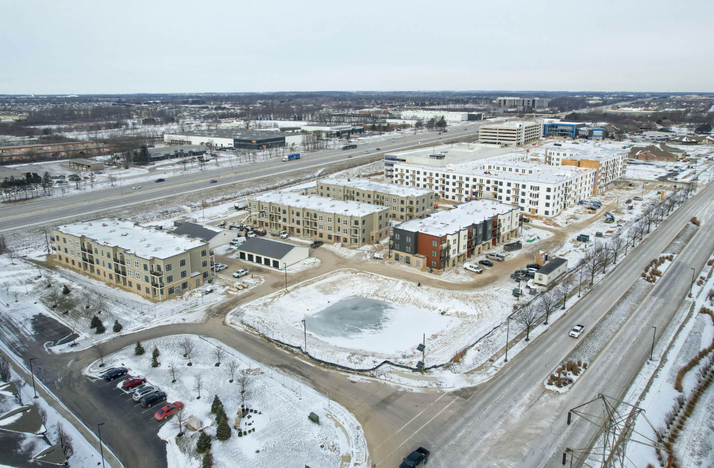 Aerial winter view of a mixed-use real estate development under construction with multi-story residential and commercial buildings surrounded by snow-covered ground.
