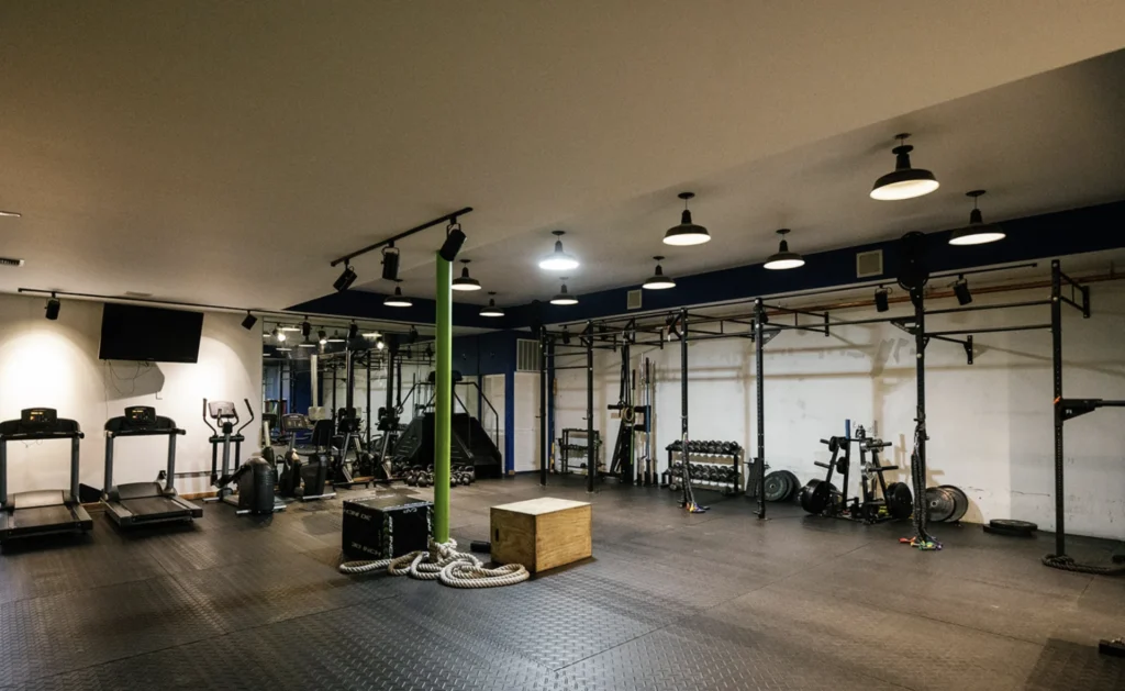 Spacious CrossFit-style gym with treadmills, pull-up rigs, plyo boxes, battle ropes, and free weights on rubber flooring.