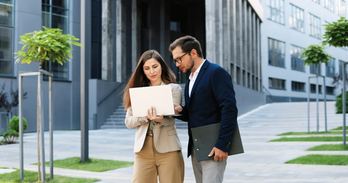 Commercial real estate professionals reviewing a project on a laptop outside an office building